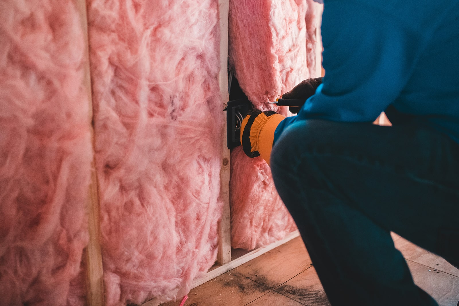 A building contractor packs pink wool insulation into a cavity wall