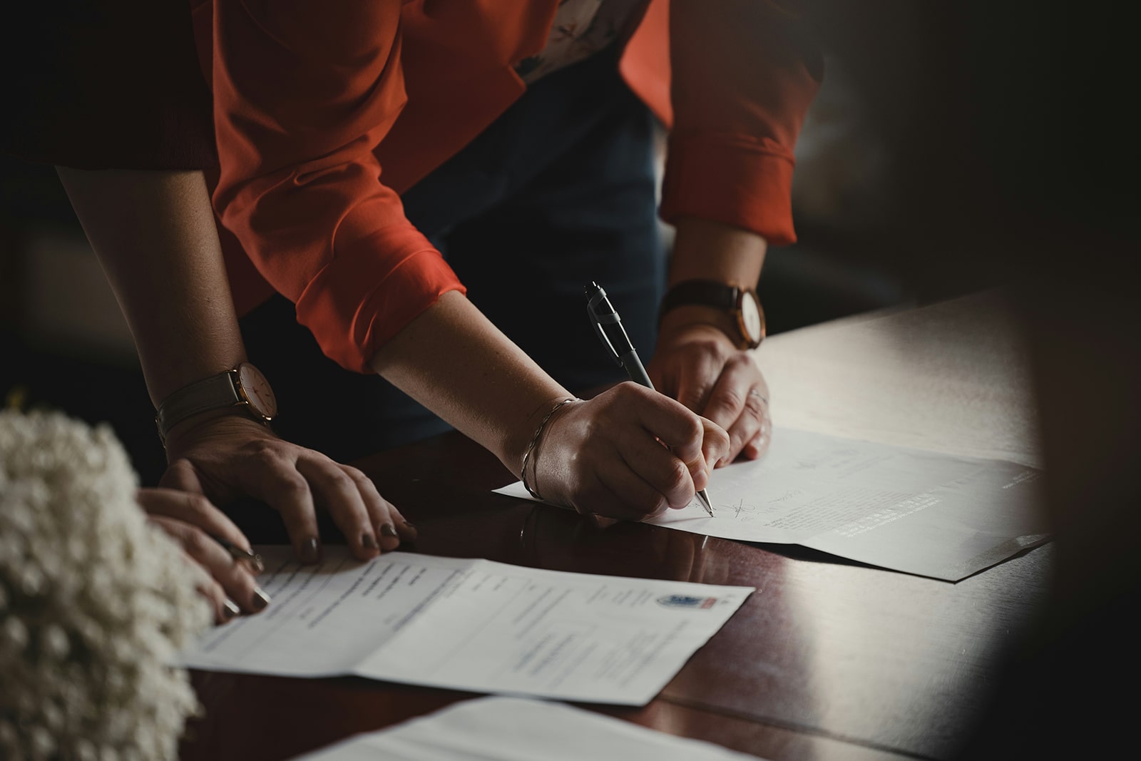 Two smartly-dressed women in a boardroom, one signs an official looking document