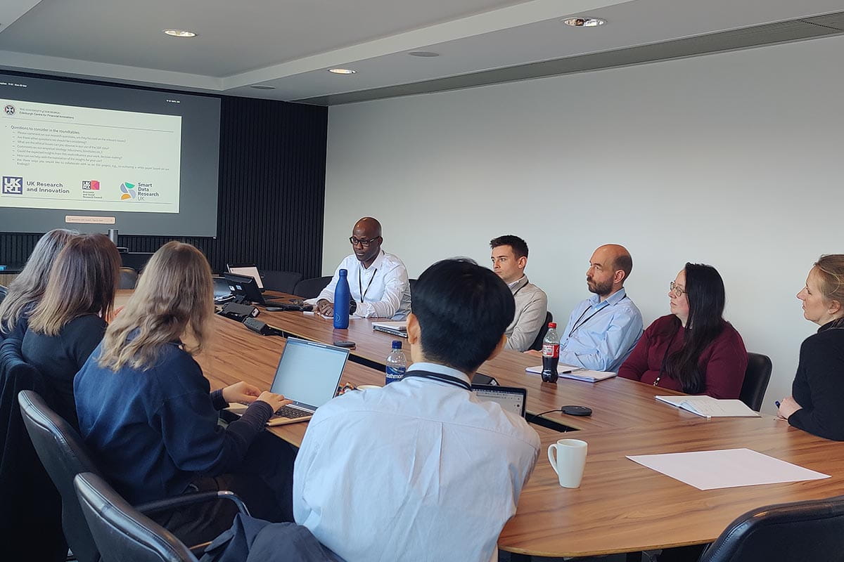 Nine people sitting around table watching a presentation on a large screen
