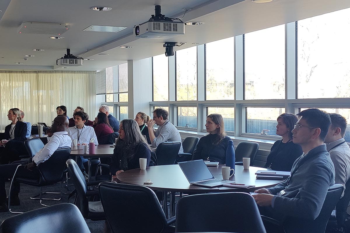 Thirteen people sitting around three tables listening to a presentation at a workshop