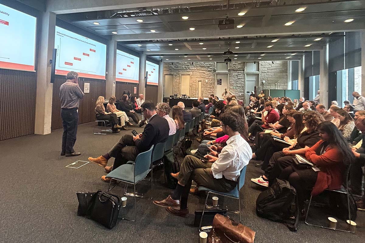 Side-on view of rows of attendees watching a presentation with speaker and panel